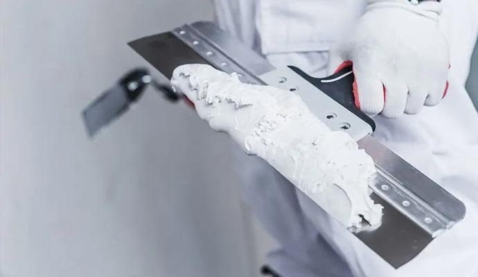 a uniformed worker appling putty to the drywall ceiling