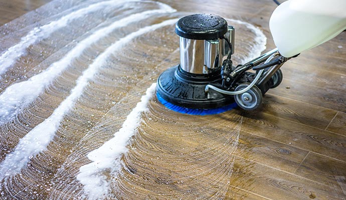 A floor cleaning machine restoring a wood floor by deep cleaning and renewing the surface without heavy sanding.