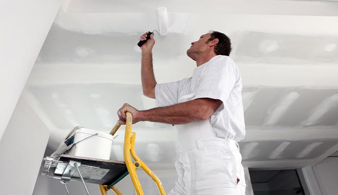A painter applying white paint to a room ceiling