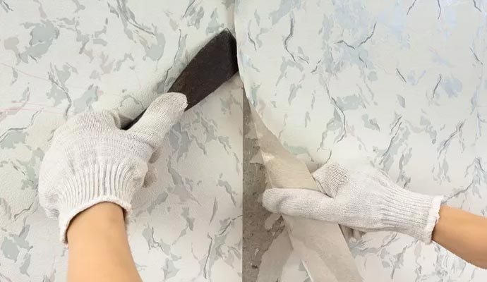 A person removing old wallpaper with a scraper tool