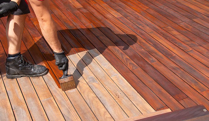 A professional applying wood stain to a deck surface, enhancing color while ensuring even coverage and long-lasting protection.