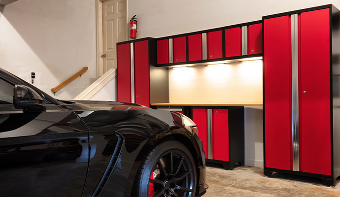 Organized garage with red cabinets and a black sports car.