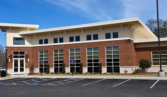 Commercial building exterior A commercial building with brick and beige siding, large windows, and a paved parking lot with marked spaces