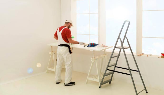 Professional painter preparing for work A painter in white overalls stands at a temporary work table, preparing his tools in a bright, white room with a large window.