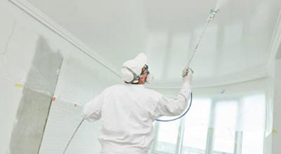painter worker with airless painting sprayer covering ceiling surface into white