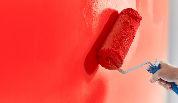 A close-up of a paint roller applying a coat of vibrant red paint to a wall.