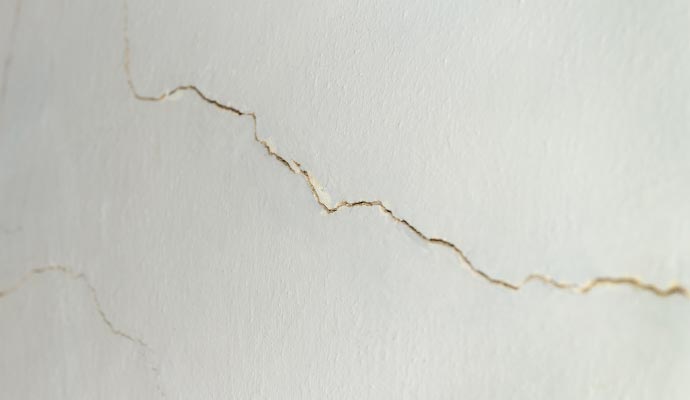 A close-up of a jagged crack running horizontally across a painted white wall.